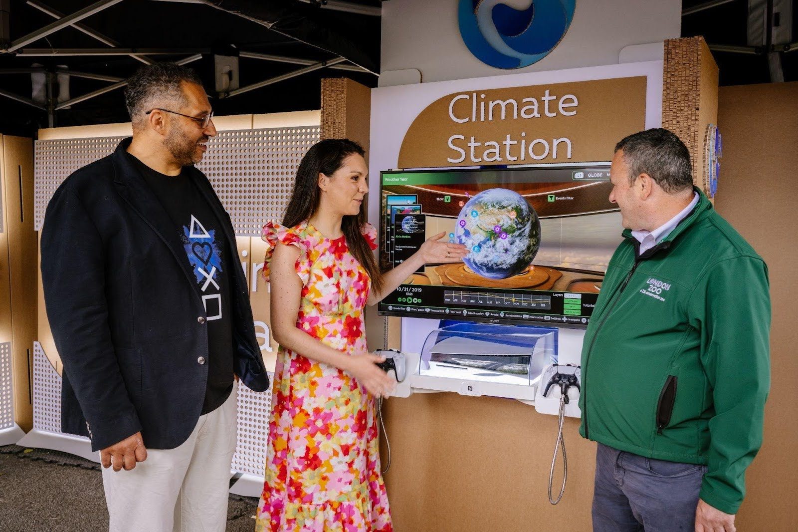 A woman and two men gathered around a showcase of the Climate Station app. The woman is pointing at the screen, that is displaying an image of Earth.